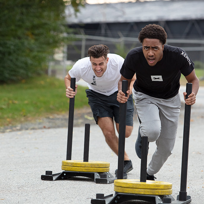 Two athletes pushing a weighted sled.