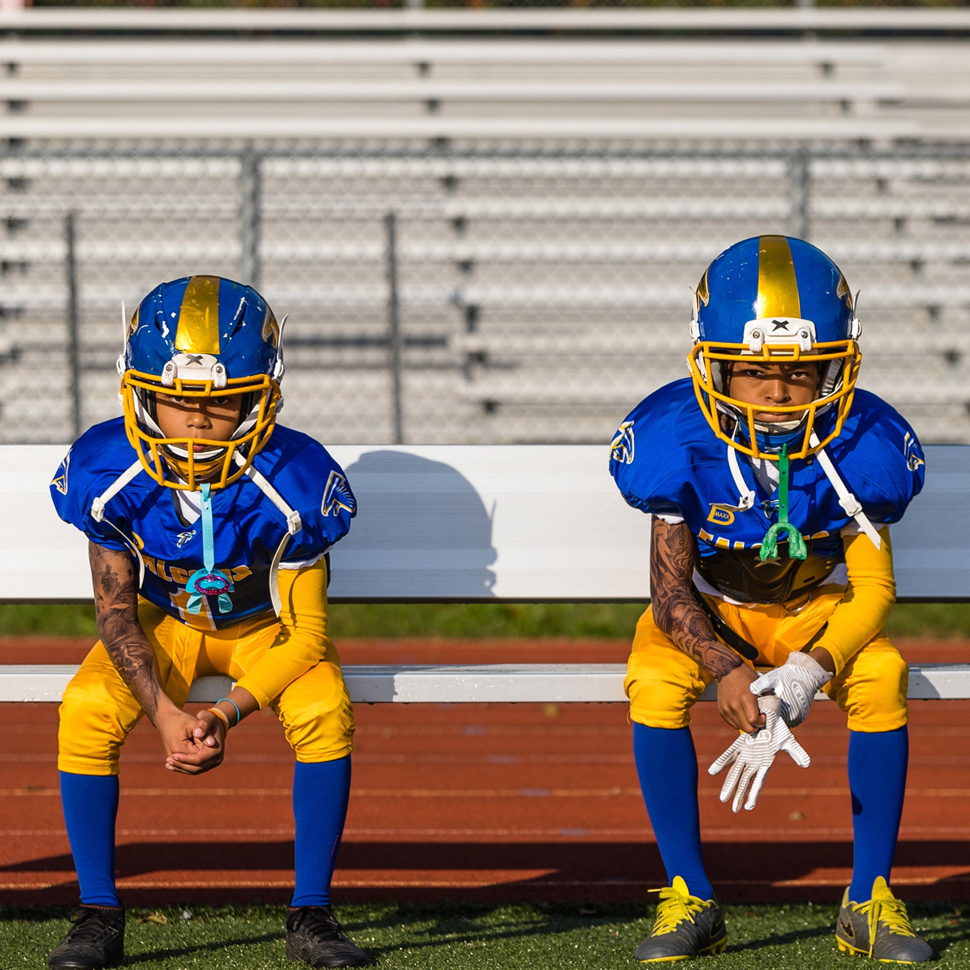 Two football players look into the camera while sitting on the bench.