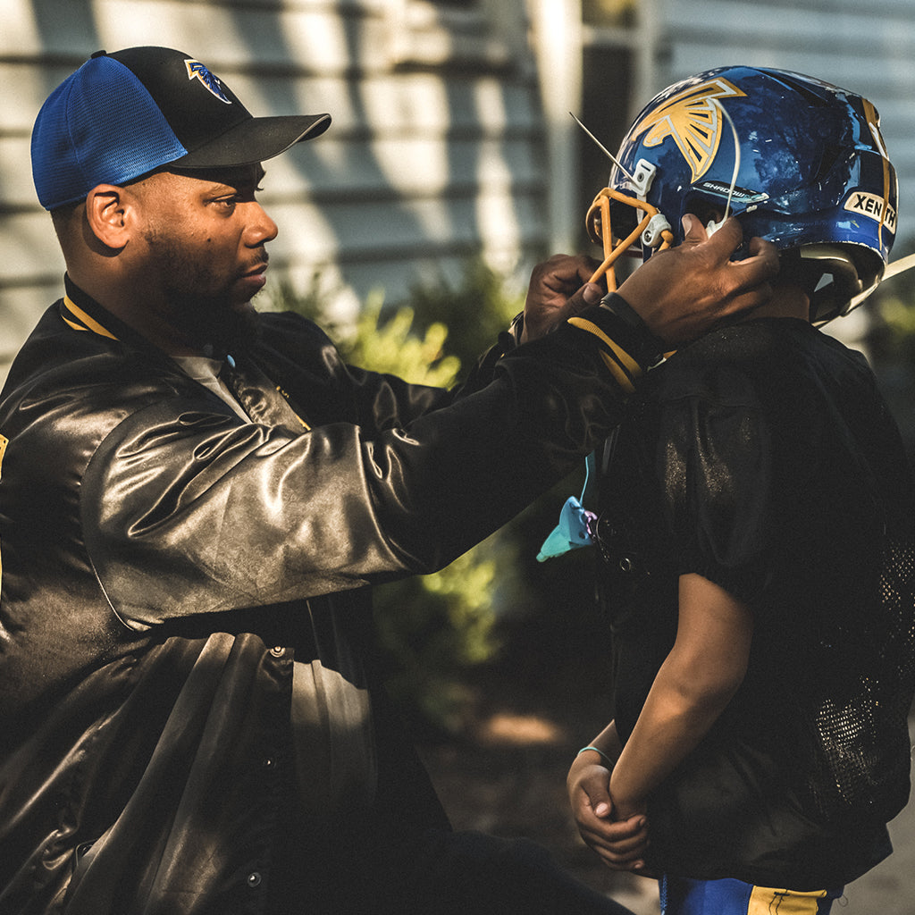 A parent fitting a helmet on a youth athlete.