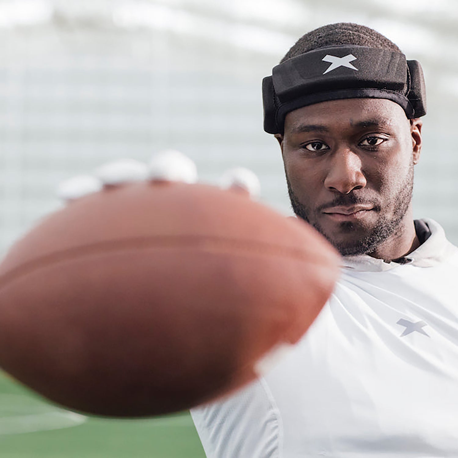 Football player wearing Xenith LOOP headgear looks into the camera holding a football.