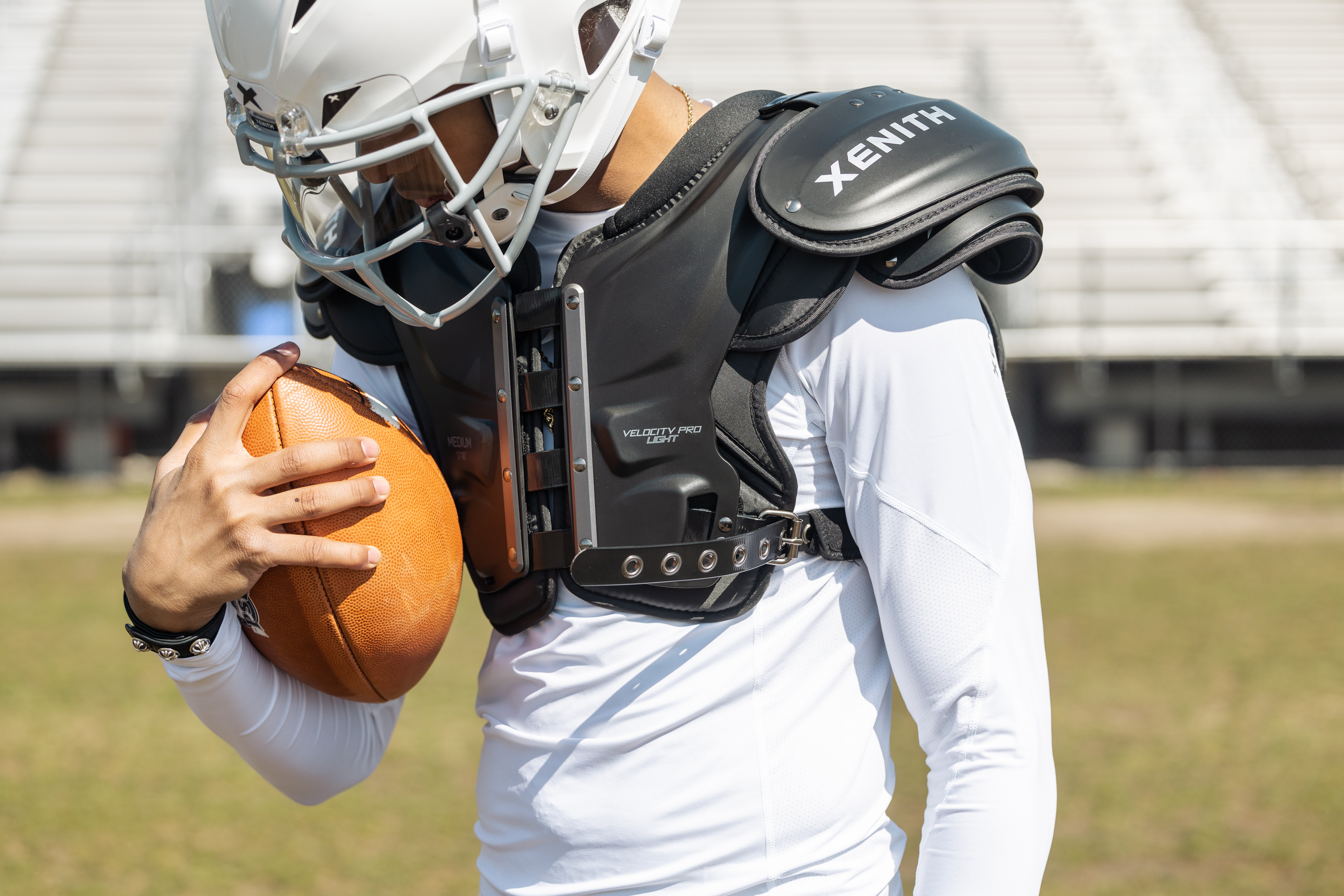 A football player wearing Xenith shoulder pads cradling a football.