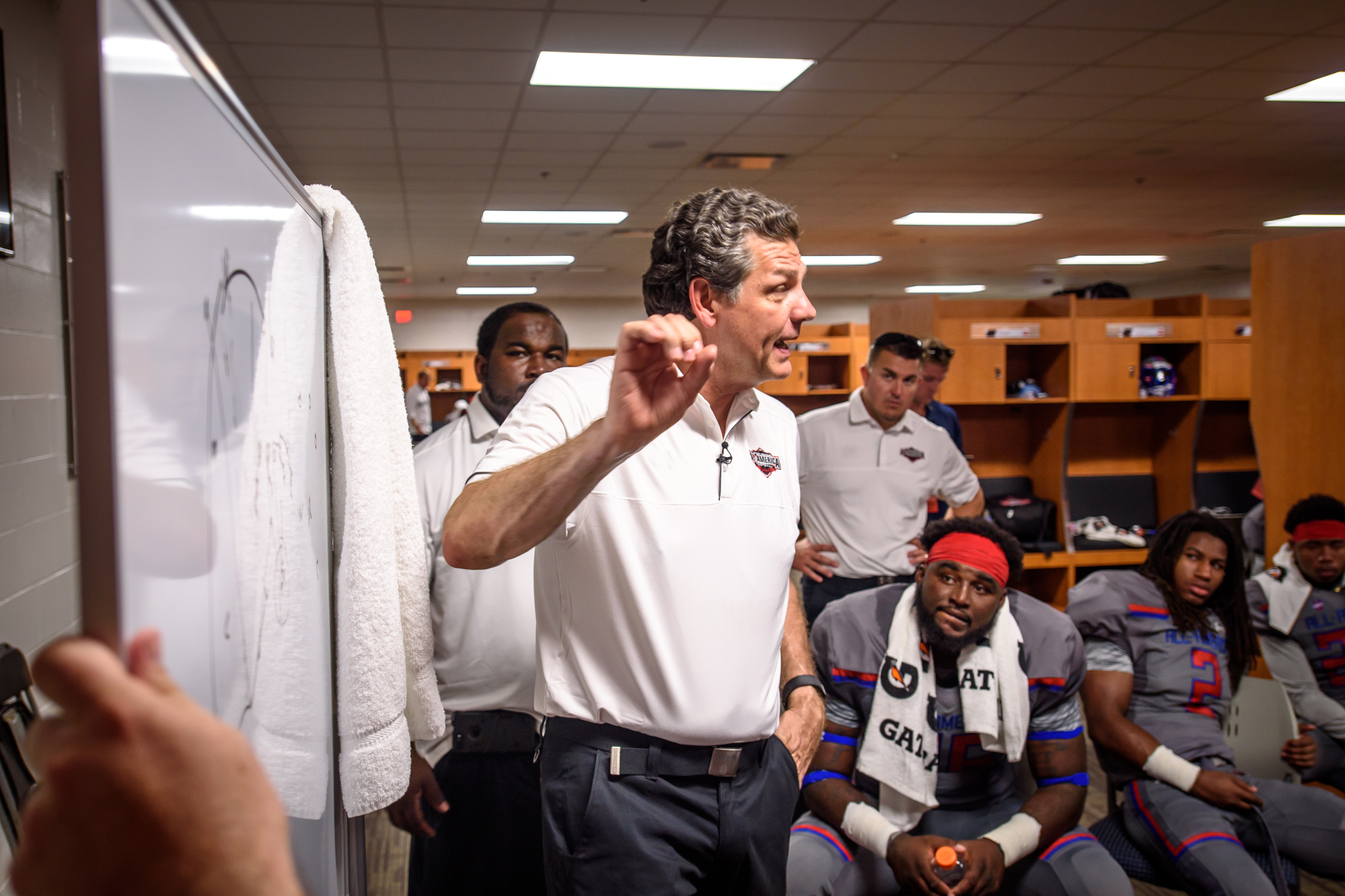 A coach pointing to a drawing board while talking to players in the locker room.