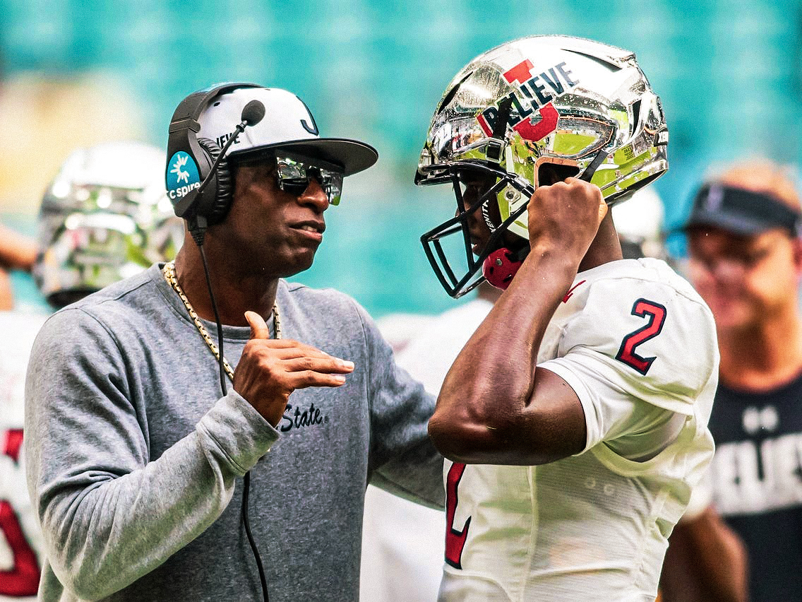 Close up of Deion Sanders talking to a player on the sideline.