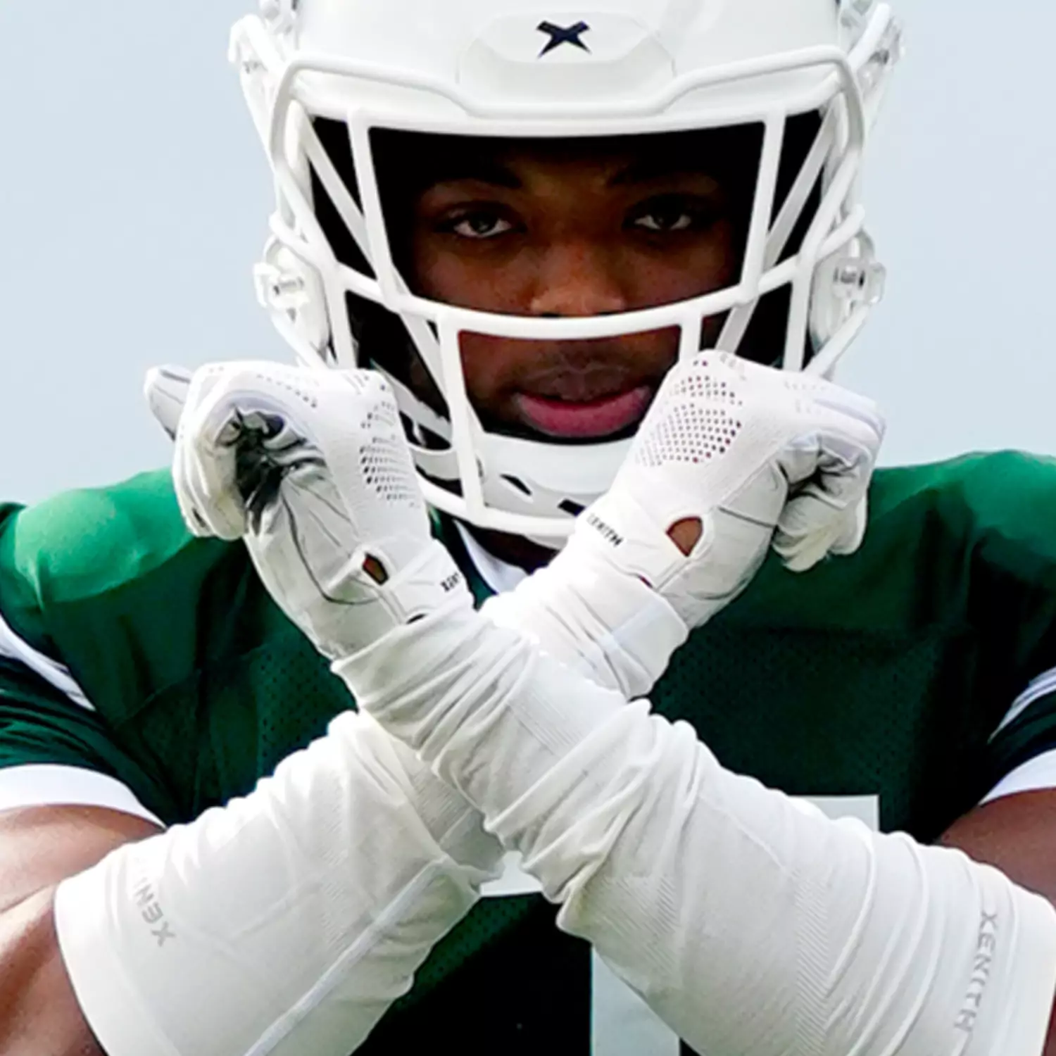Close up of Jalen Thompson holding his arms up in an X shape while wearing a white Xenith helmet.