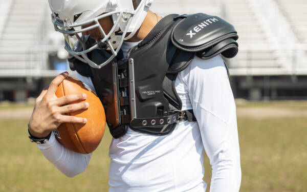 A football player wearing Xenith shoulder pads cradling a football.