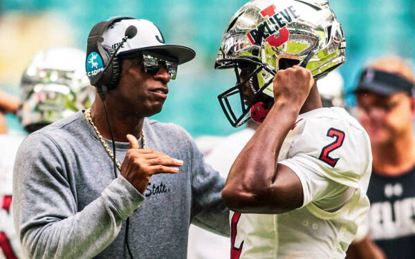 Close up of Deion Sanders talking to a player on the sideline.