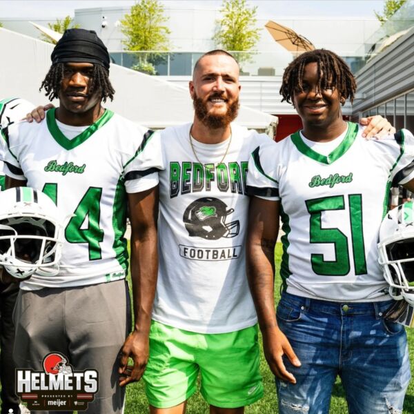 Two Bedford High School players posing with their coach and holding Xenith helmets.