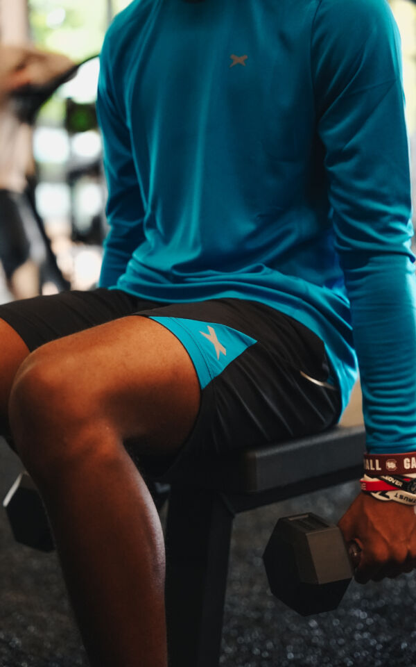 Close up of Prince sitting down holding a pair of dumbbells by his side.