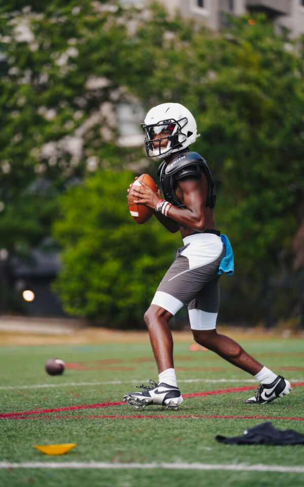 Prince holding a football while dropping back to throw a pass.