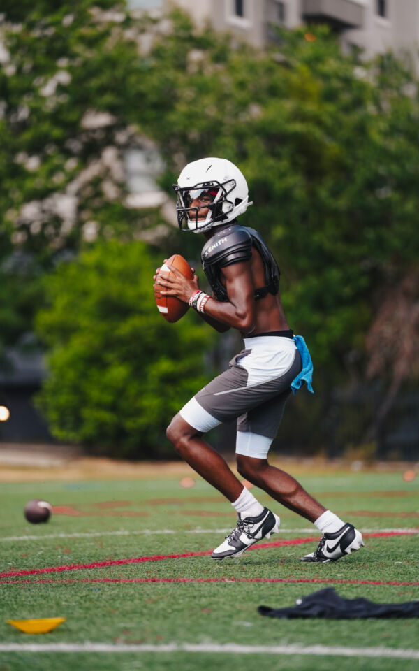 Prince holding a football while dropping back to throw a pass.